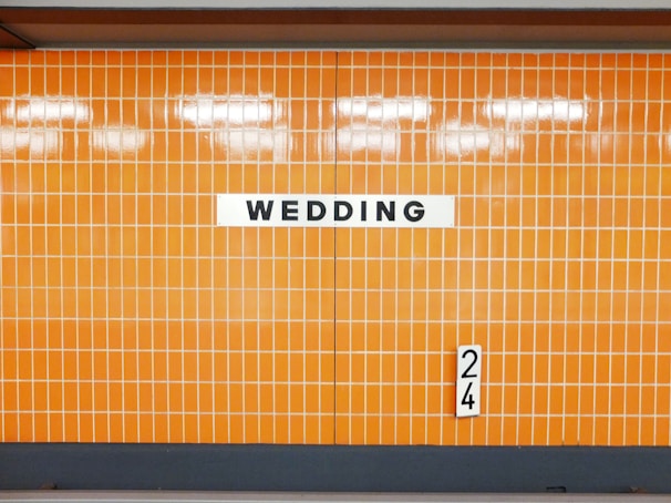An orange-tiled wall with the word 'WEDDING' prominently displayed on a white sign. A small number '24' is also visible on the right side of the wall.
