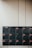 A set of sixteen black mailboxes arranged in a four by four grid is mounted on a light-colored wall. Each mailbox has a label with red accents that indicate unit numbers. The overall setting is minimal and organized.