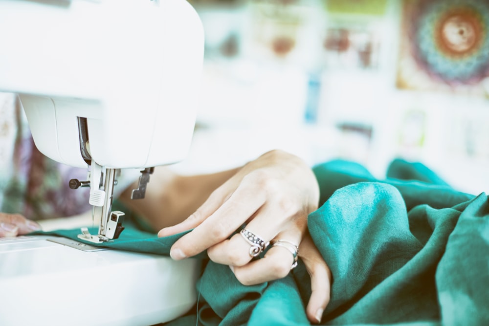 person sewing green textile using white electric sewing machine