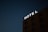 A dark night sky serves as the backdrop to an illuminated sign that reads 'HOTEL' affixed to the top of a multi-story building. The building is mostly in shadow, with outlines of windows visible.