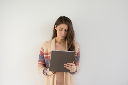 Brown-haired woman standing in front of a white wall using a grey tablet.