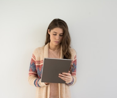 woman in beige, gray, and red sweater holding silver tablet computer