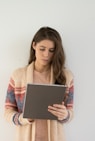 woman in beige, gray, and red sweater holding silver tablet computer