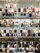 A multi-level clothing store interior featuring numerous shelves and mannequins displaying various garments. Clothes of different colors, including shirts, sweaters, and jackets, are arranged neatly. The store has bright lighting, and there are shoppers visible in some sections.