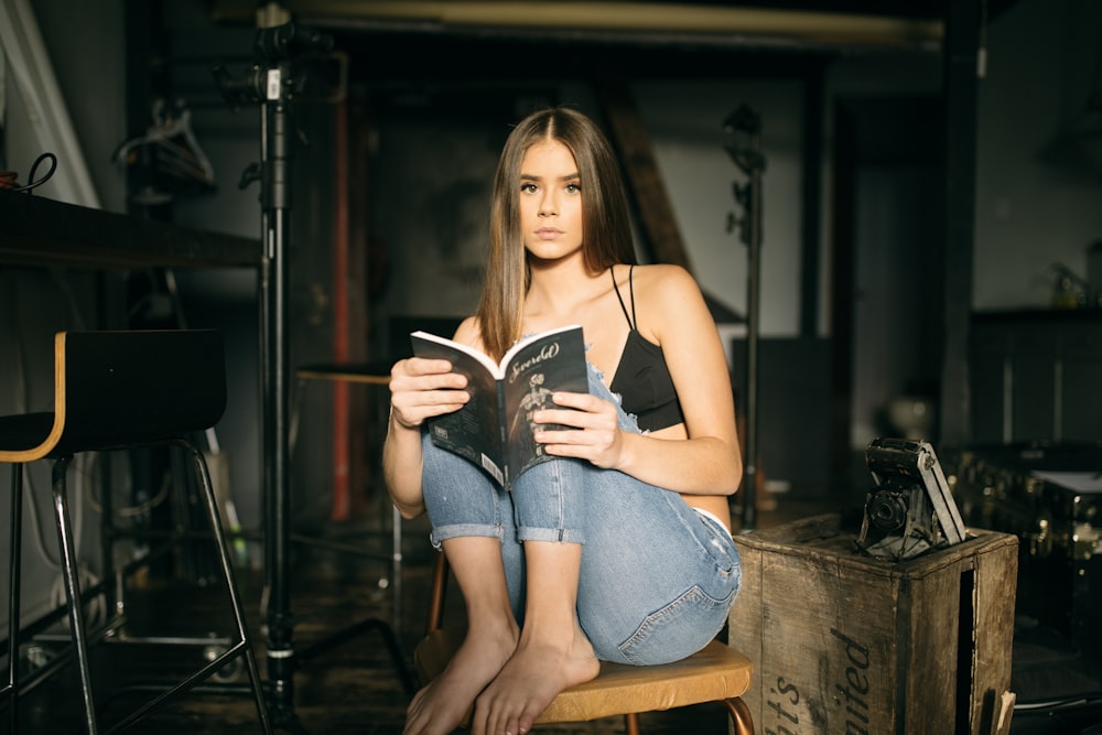 Mujer sentada en una silla marrón mientras lee un libro dentro de una habitación bien iluminada