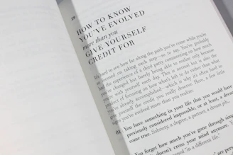 An open book is displayed with a visible page featuring large bold text at the top reading 'HOW TO KNOW YOU'VE EVOLVED more than you GIVE YOURSELF CREDIT FOR.' Below is a paragraph discussing personal growth and self-reflection, encouraging readers to acknowledge their achievements.