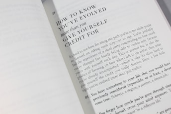An open book is displayed with a visible page featuring large bold text at the top reading 'HOW TO KNOW YOU'VE EVOLVED more than you GIVE YOURSELF CREDIT FOR.' Below is a paragraph discussing personal growth and self-reflection, encouraging readers to acknowledge their achievements.