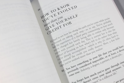 An open book is displayed with a visible page featuring large bold text at the top reading 'HOW TO KNOW YOU'VE EVOLVED more than you GIVE YOURSELF CREDIT FOR.' Below is a paragraph discussing personal growth and self-reflection, encouraging readers to acknowledge their achievements.