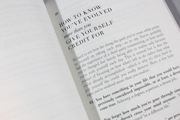 An open book is displayed with a visible page featuring large bold text at the top reading 'HOW TO KNOW YOU'VE EVOLVED more than you GIVE YOURSELF CREDIT FOR.' Below is a paragraph discussing personal growth and self-reflection, encouraging readers to acknowledge their achievements.