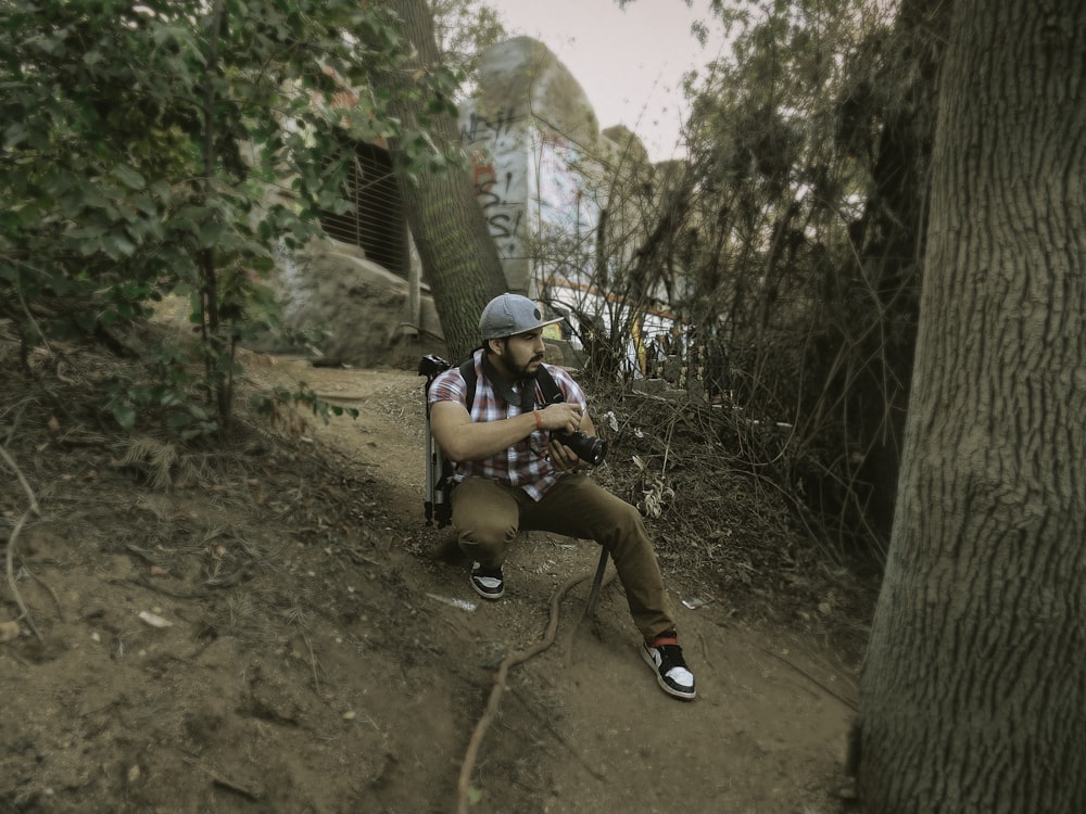 man sitting on ground beside trees and plant during daytime