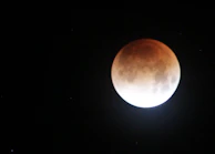 A lunar eclipse partially covering the full moon in dramatic darkness.