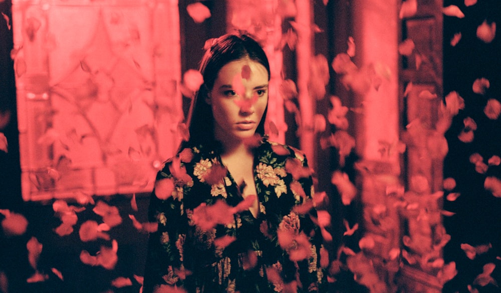 woman wearing black and multicolored dress standing while red flower petals falling from above photo