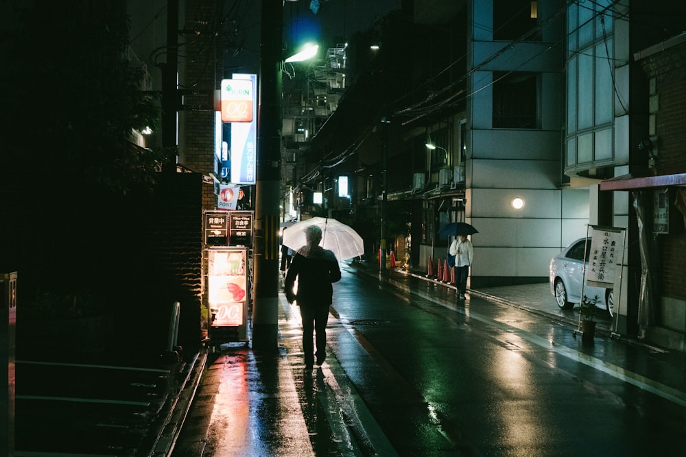 persona che tiene l'ombrello vicino all'edificio durante la notte