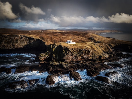 white house on the top of brown mountain near body of water during daytime in Stoer Lighthouse United Kingdom