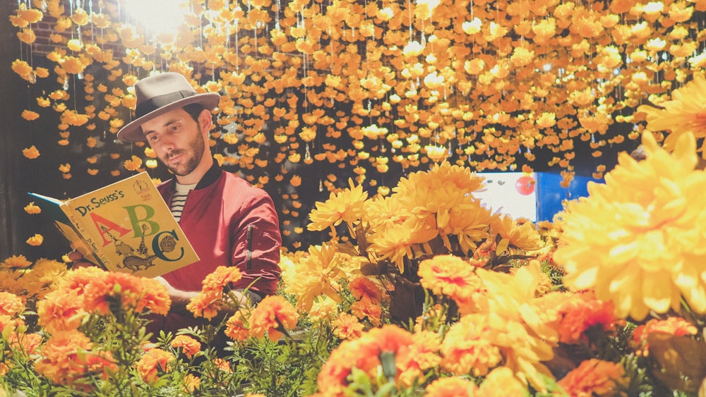 Hombre leyendo un libro cerca de flores amarillas