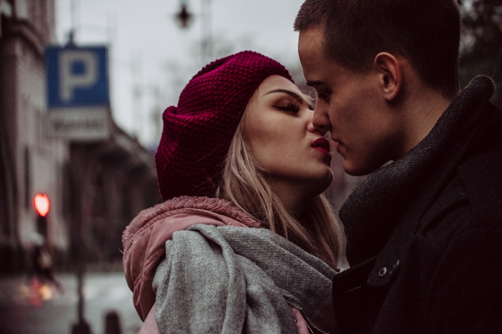 man and woman standing while kissing beside street signage