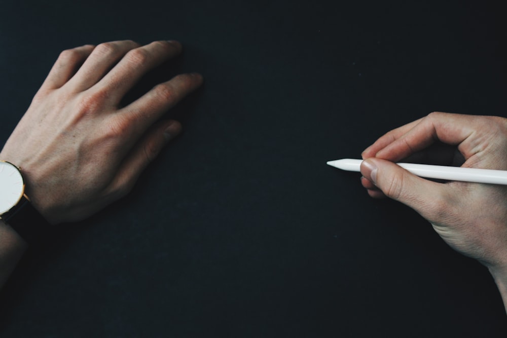 person wearing black analog watch holding white pencil