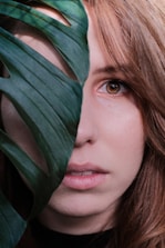woman face behind green Swiss cheese plant