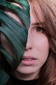 woman face behind green Swiss cheese plant