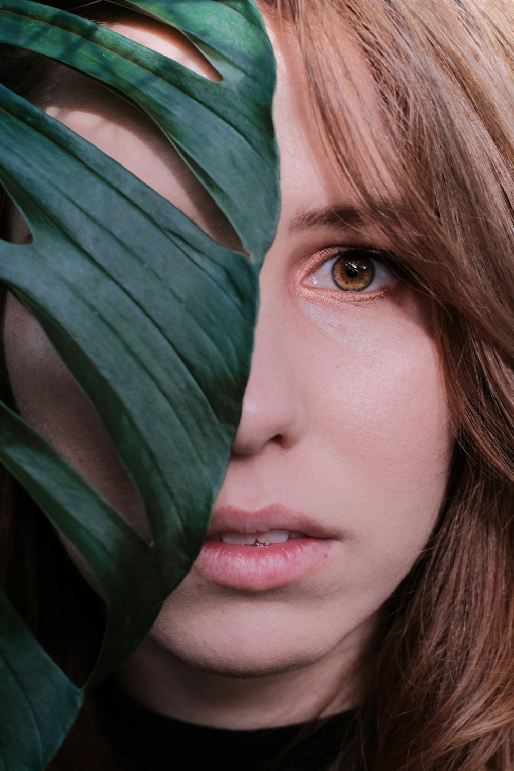 woman face behind green Swiss cheese plant