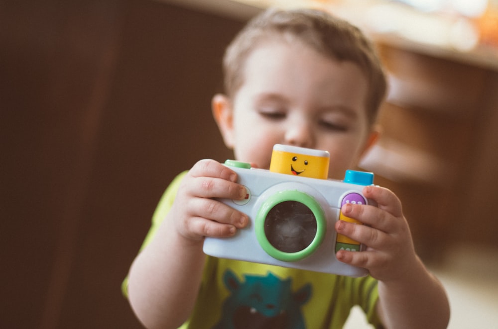 enfant en bas âge tenant un jouet de caméra blanc