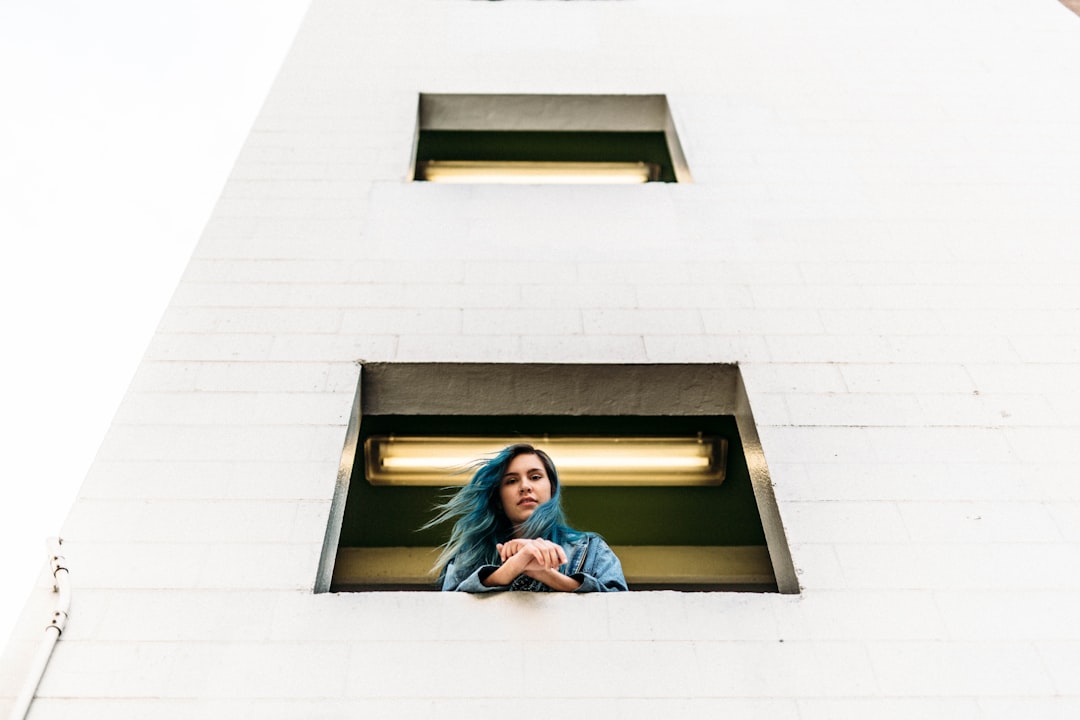 blue haired woman on window on white concrete building during daytime