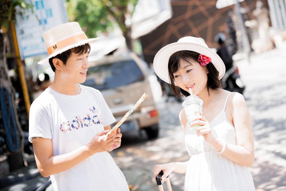 man and woman wearing hats holding disposable cups near vehicle during daytime