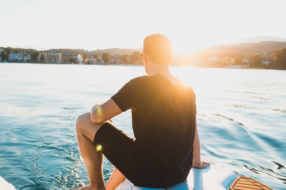 man wears black sits on floating object in middle of body of water during daytime