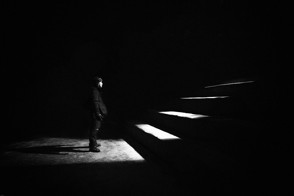 grayscale photo of man standing in front of stairs