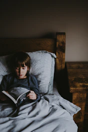 Happy child reading a picture book under a cozy blanket fort