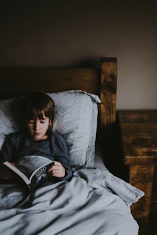 Happy child reading a picture book under a cozy blanket fort