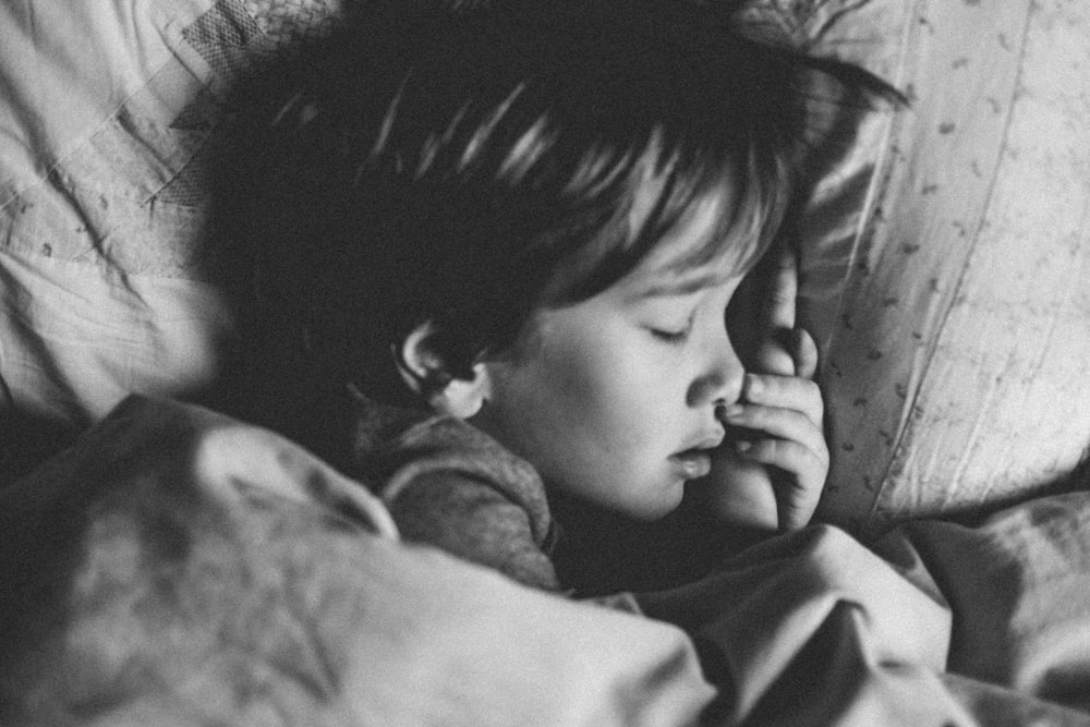 Graustufenfoto eines Mädchens, das auf weißem Kissen schläft