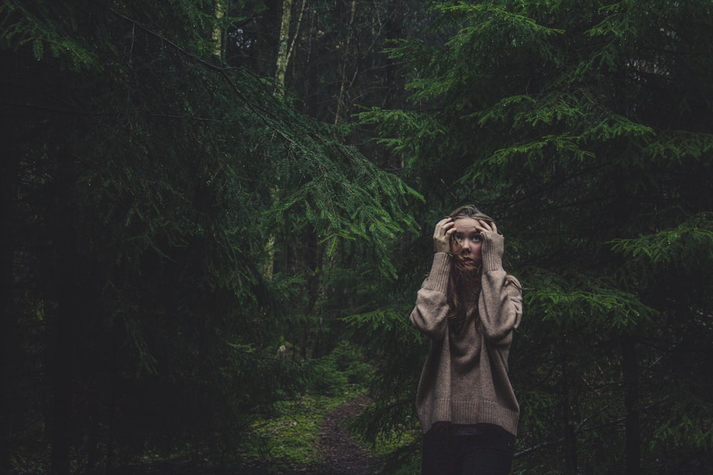 woman holding head standing between trees