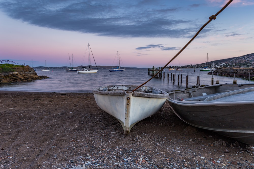 white and grey boats on sand in front of body of water