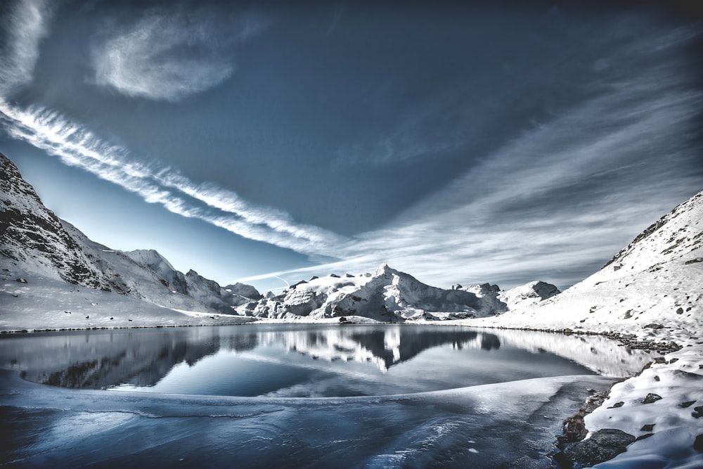 cuerpo de agua entre la cordillera cubierta de nieve bajo el cielo gris y las nubes blancas durante el día