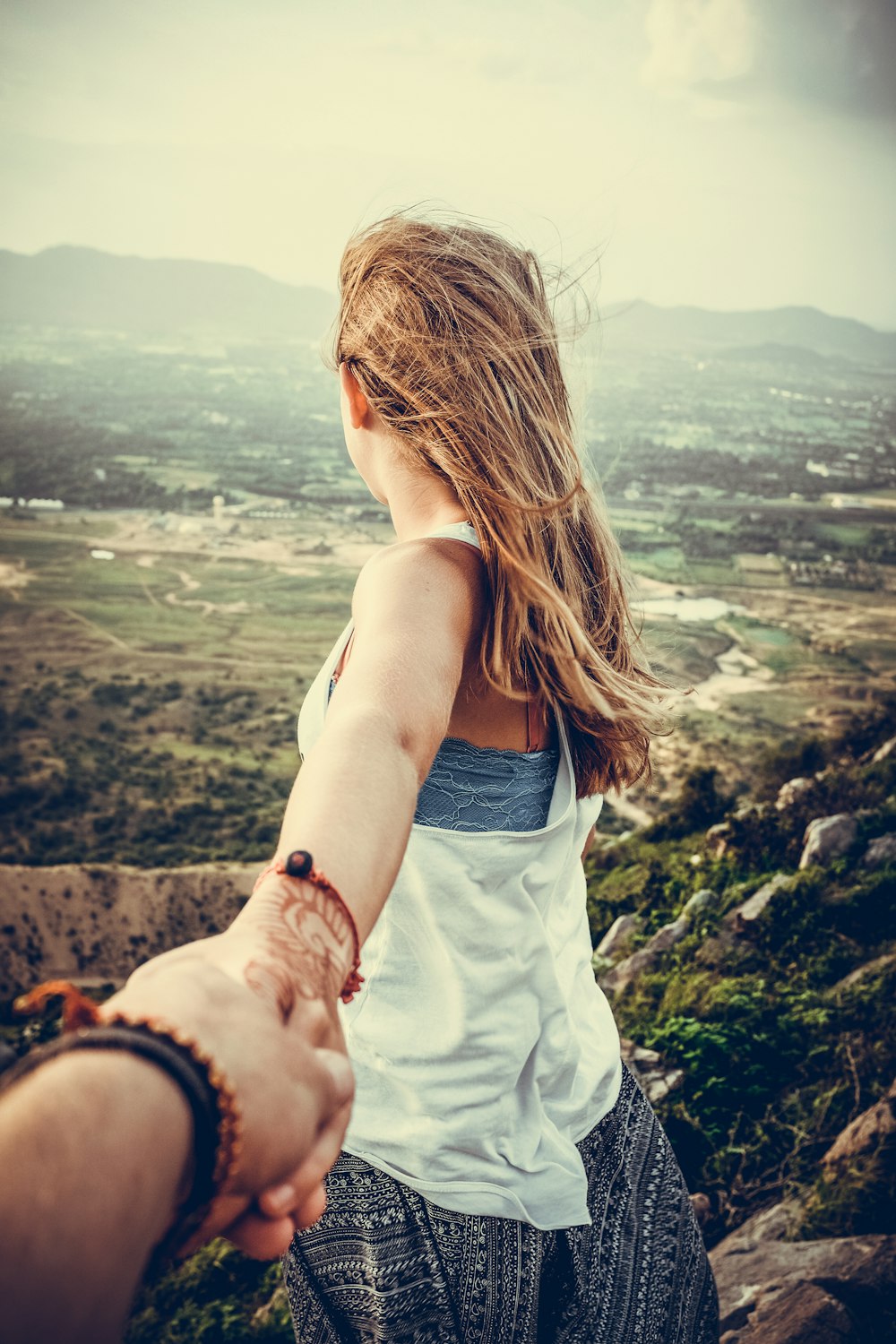 person holding woman wearing white tank top standing beside big rocks near mountain during daytime