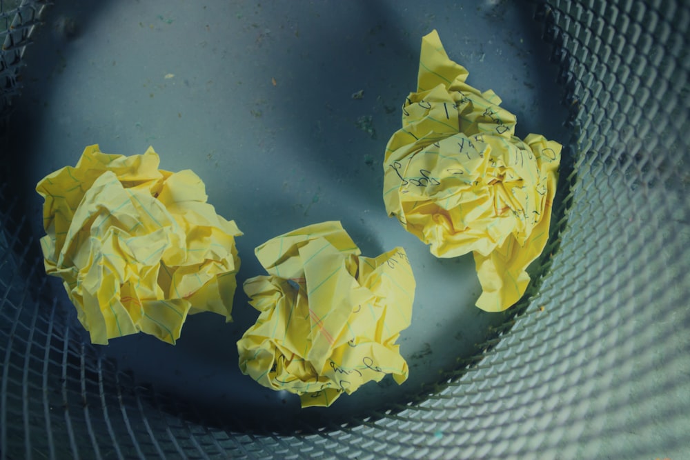 Drei gelbe, zerbröckelte Papiere in einem grauen Mülleimer