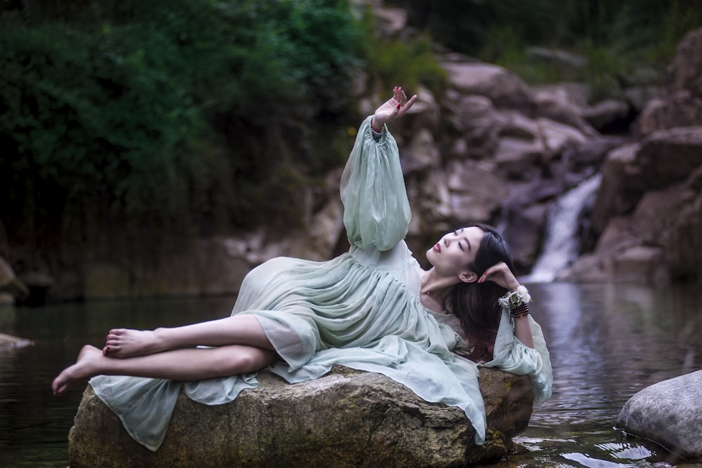 woman lying on large stone between flowing river
