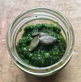 An elegant jar of green-hued pumpkin seed butter resting on a stone surface with whole seeds artfully placed nearby.