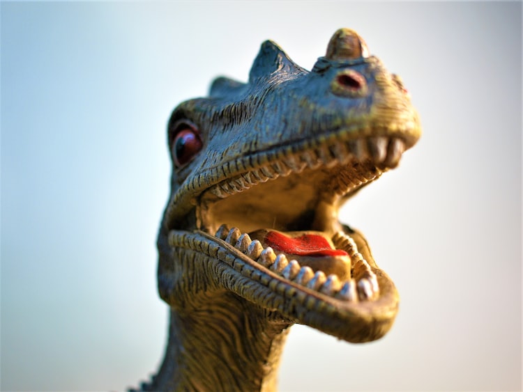 Close up on a toy carnivorous dinosaur with its mouth open, it has red eyes and a red tongue