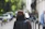 Man in a matte black jacket carrying a sleek espresso brown leather messenger bag in a cityscape setting.