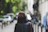 Man in a matte black jacket carrying a sleek espresso brown leather messenger bag in a cityscape setting.