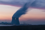 skyline photography of nuclear plant cooling tower blowing smokes under white and orange sky at daytime