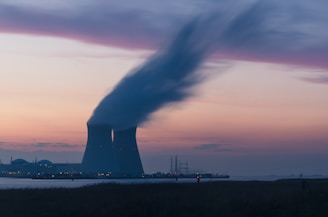 skyline photography of nuclear plant cooling tower blowing smokes under white and orange sky at daytime
