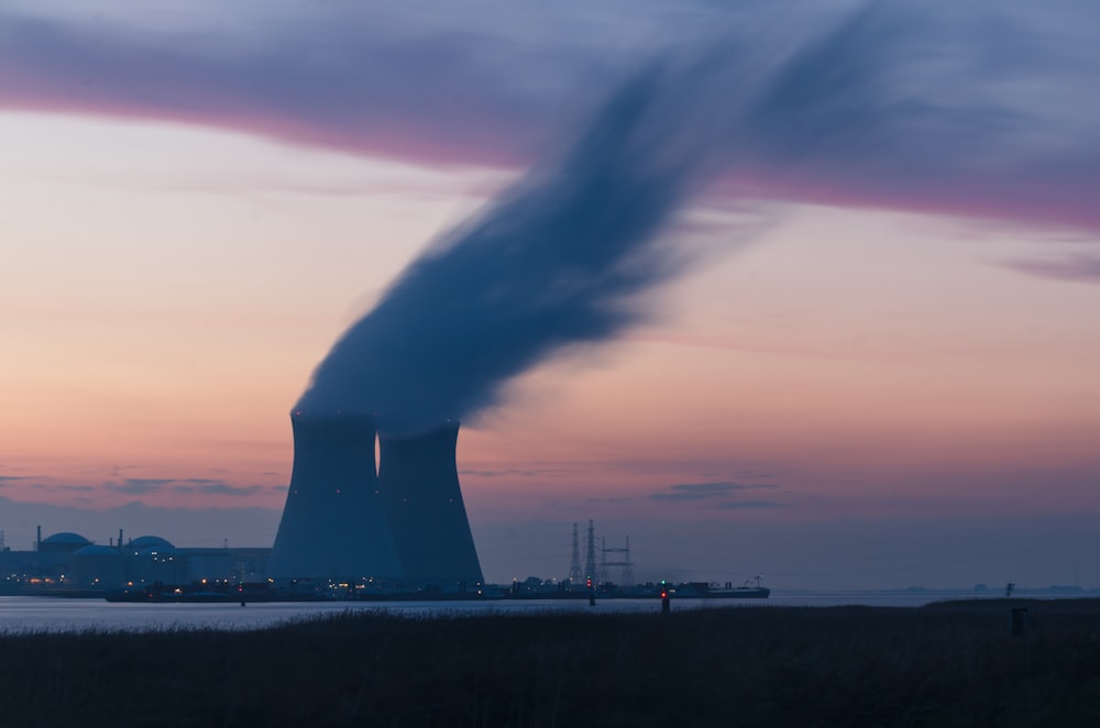 Fotografía del horizonte de la torre de enfriamiento de la planta nuclear que sopla humos bajo el cielo blanco y naranja durante el día