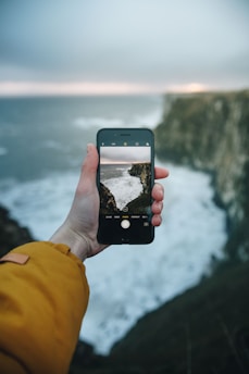 person holding phone taking picture of ocean wave