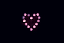 A glowing candle surrounded by delicate pink and red hearts glowing warmly.