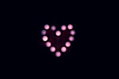 A glowing candle surrounded by delicate pink and red hearts glowing warmly.