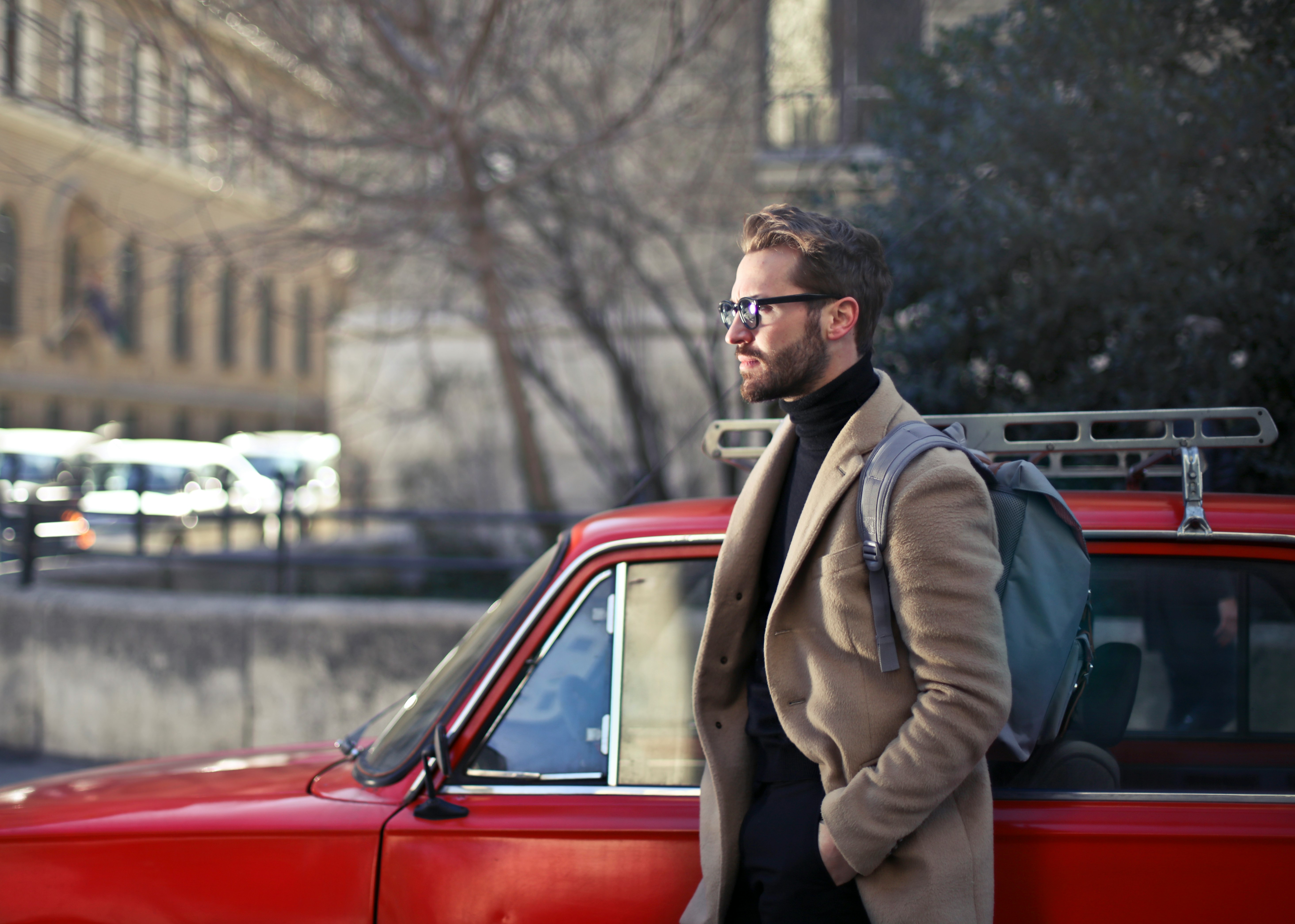 man on beige coat standing beside red car