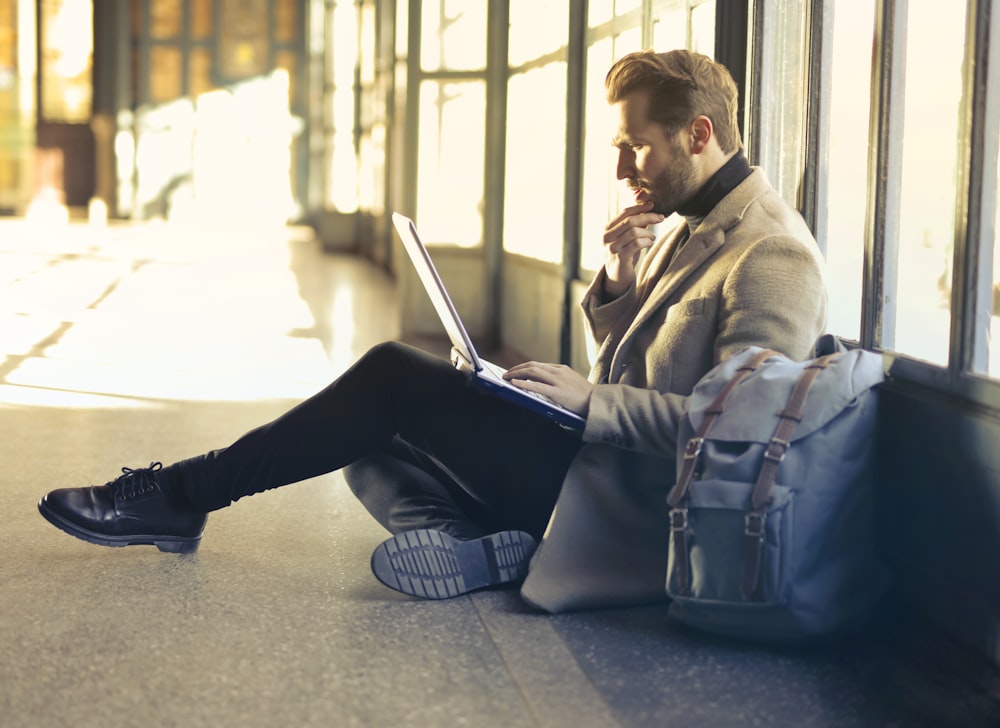 man sitting on floor while using laptop